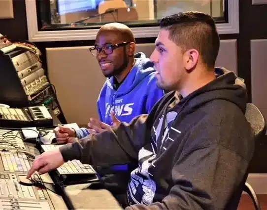 Two men in front of a monitor and a sound board to illustrate how do become a sound effecrs editor