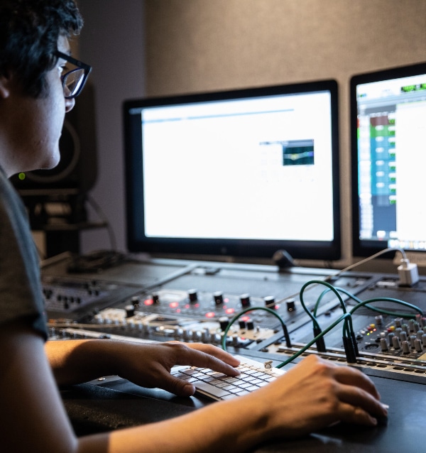 A sound effects editor in front of a monitor and some gear