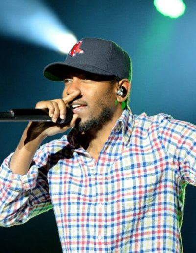 Kendrick Lamar wearing a baseball cap and holding a microphone while performing on stage.
