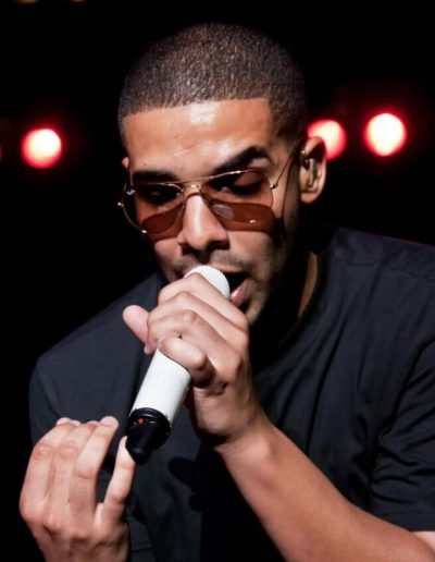Drake singing into a microphone with red stage lights in the background.