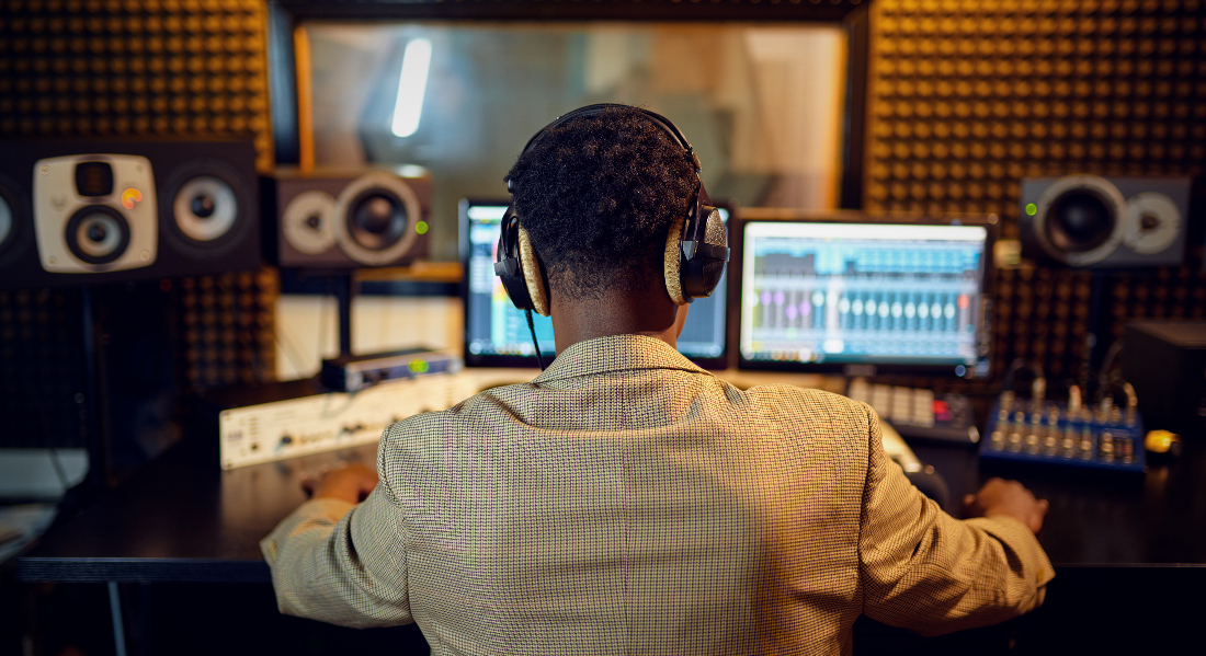 Male sound engineer at mixing console, back view, inside a recording studio to illustrate Navigating the Music Industry in Los Angeles: Insights for Audio Engineers.
