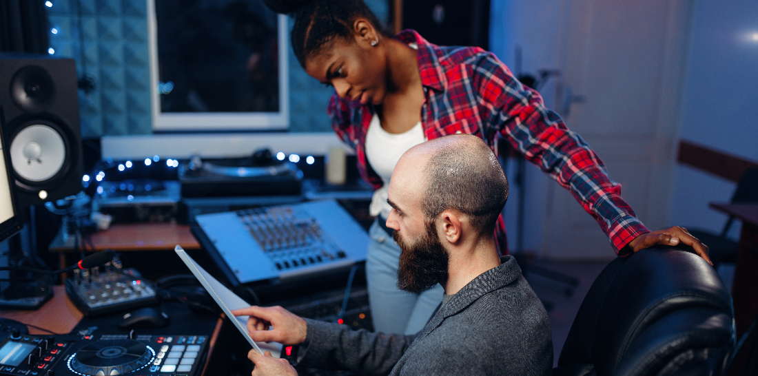 Bearded sound engineer at remote control panel in audio recording studio talking with a woman to help illustrate Should You Move to Los Angeles for Music Production